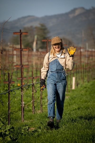 A team member at Eco Terreno is waving a hand at the camera while pruning the vines in winter time.