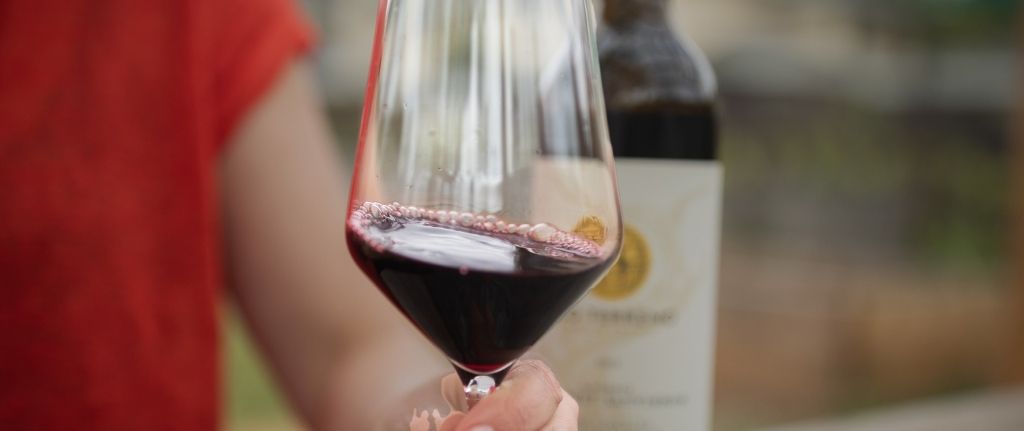 Red wine from Alexander Valley in a glass with a person holding the glass and wine bottle in the background