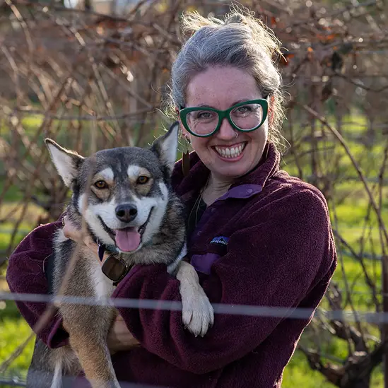Nicole Tracy, Eco Terreno Vineyard Manager holding her dog, while standing in the vineyards